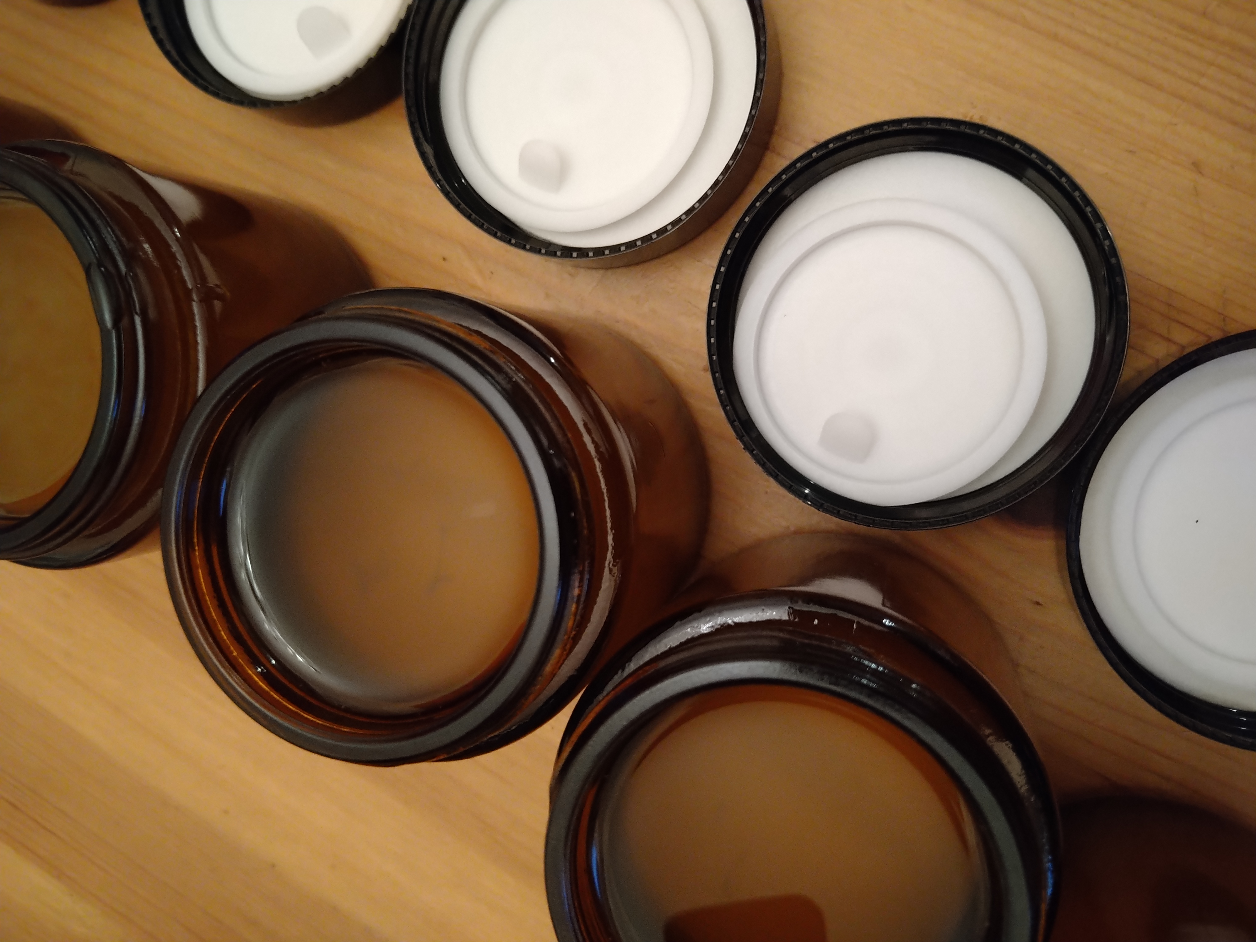 Cremedosen gefüllt mit Schafcreme geöffnet auf einem Tisch. Die Creme ist noch nicht erkaltet und daher noch transparent flüssig.